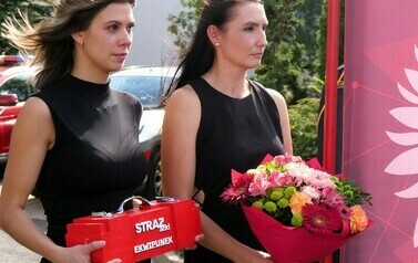 Przejście na emeryturę st. bryg. Leszka Zielińskiego (zdjęcie przedstawia dwie kobiety, jedna niosąca prezent, natomiast druga bukiet kwiat&oacute;w)