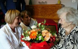 Sto lat Pani Krystyny Bassara (na zdjęciu znajduje się kobieta wręczajaca kwiaty drugiej kobiecie)
