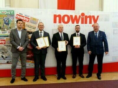 kilka osób trzymających statuetki i dyplomy, nad nimi napis nowiny